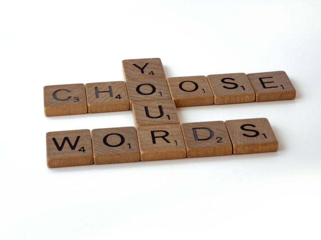 Bild besteht aus einer Anordnung hölzerner Scrabble-Elemente auf weißem Hintergrund, die zusammengelegt die Aussage ergeben: Choose Your Words; Photo by @brett_jordan on Unsplash